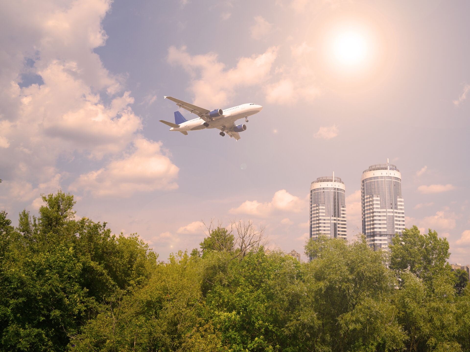 Plane flying over trees with two skyscrapers in background.