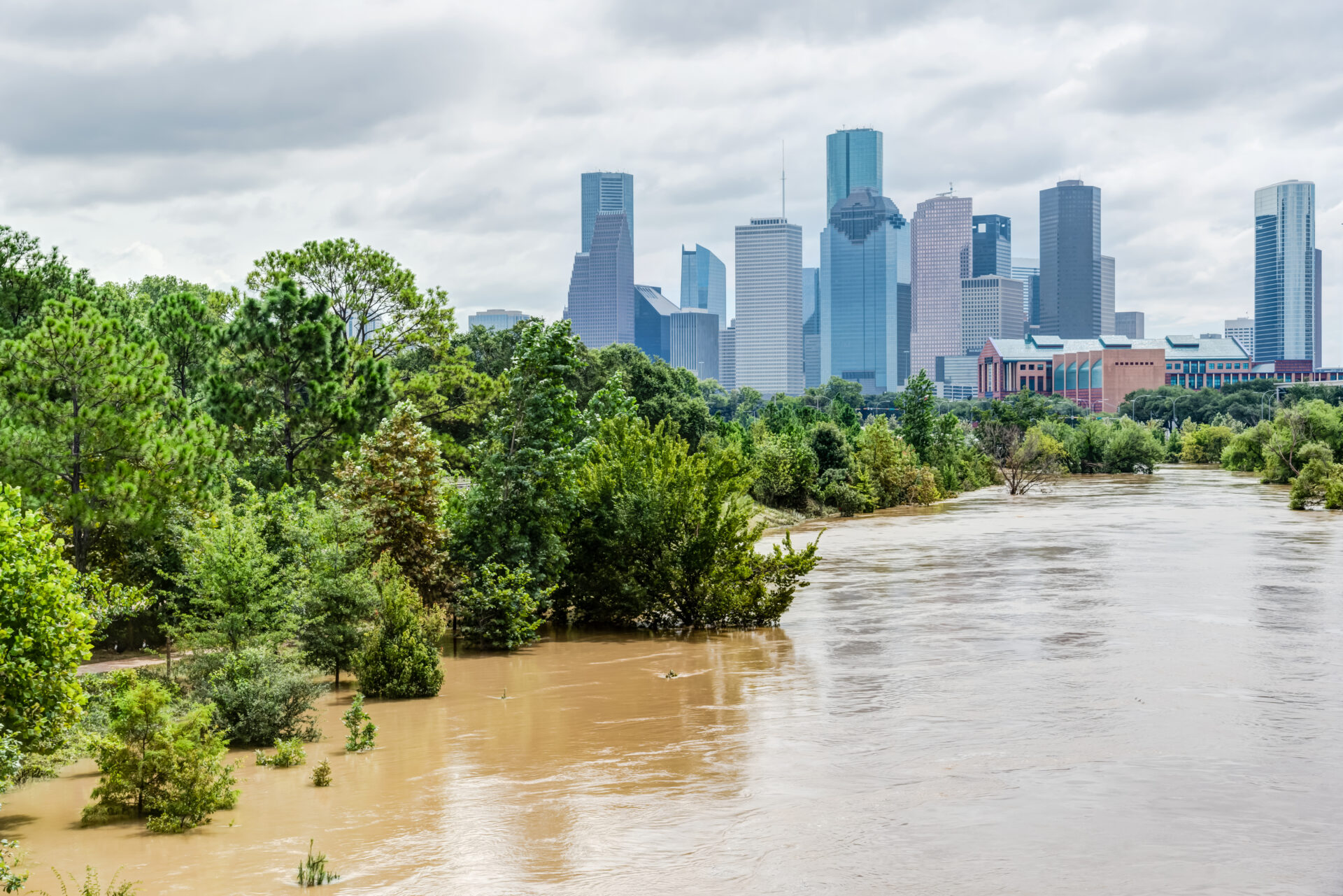 High and fast water rising in Bayou River with downtown Houston in background under cloud blue sky. Heavy rains from Harvey Tropical Hurricane storm caused many flooded areas in greater Houston area.